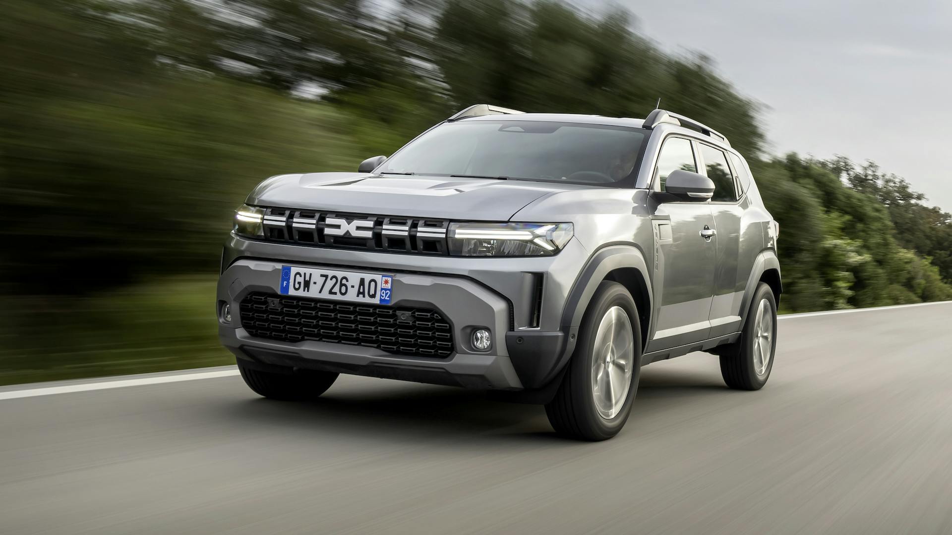 Grey 2024 Dacia Duster driving in the countryside, front quarter view.